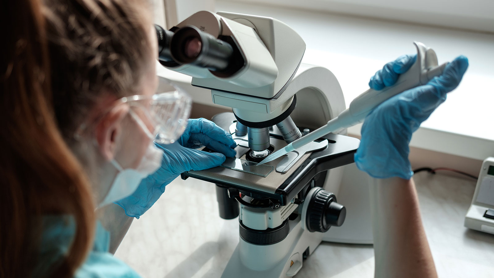 woman working with microscope holding automatic pipette